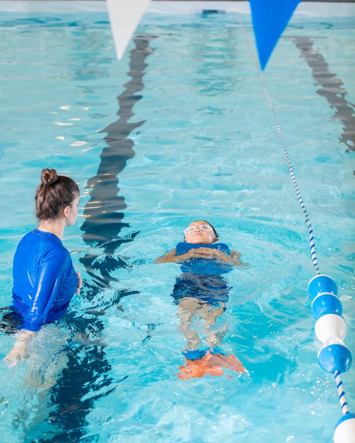 A swimming instructor teaches a young child to swim in an indoor pool.