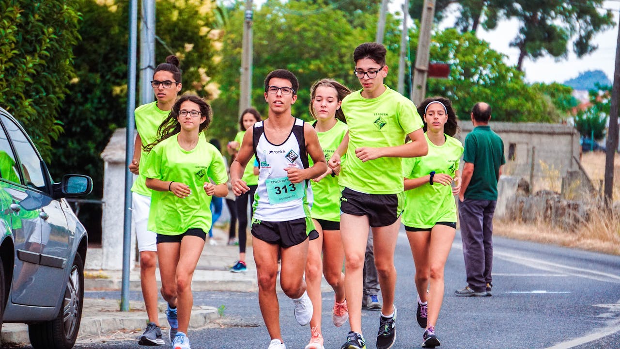 A group of young joggers running together on a road in bright green shirts, showcasing team effort.