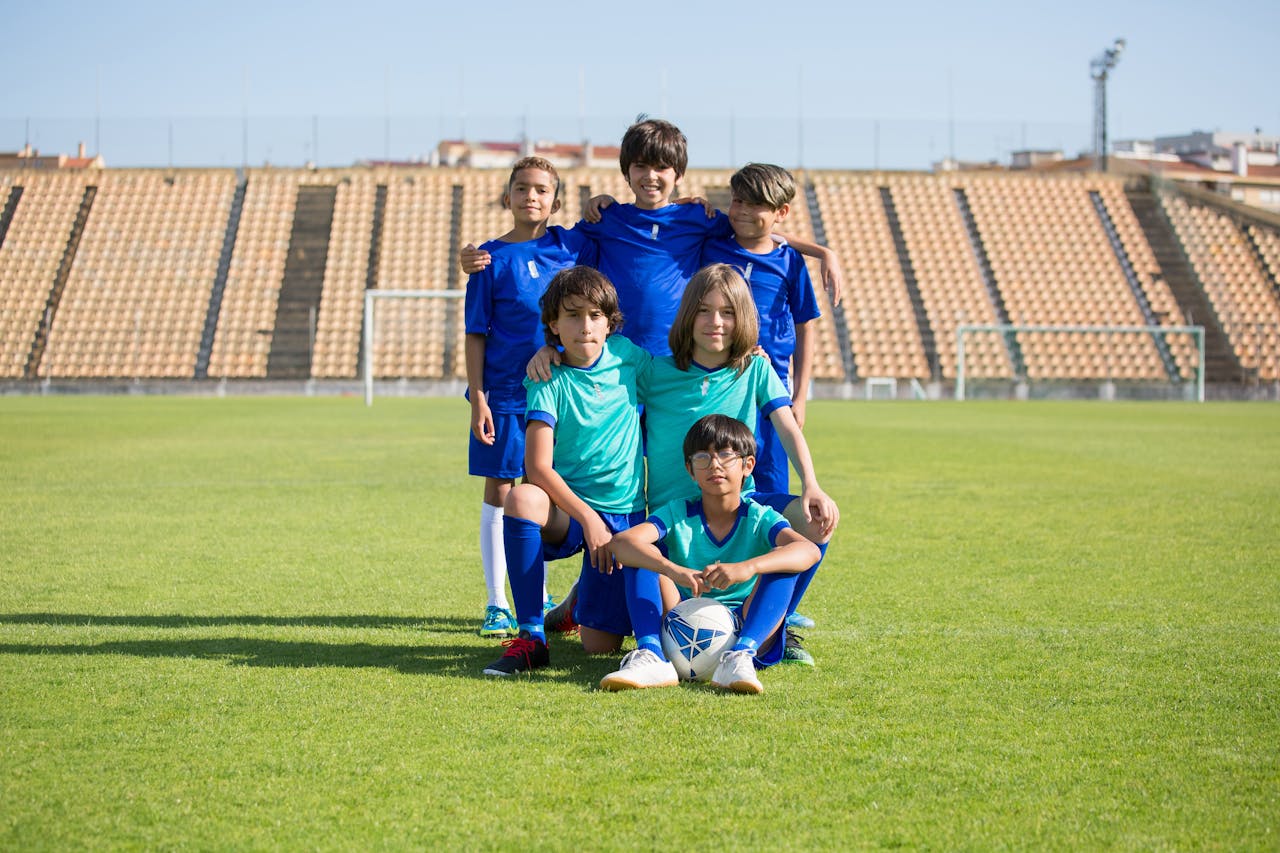 Group of young boys in soccer uniforms posing with a ball on a football field.